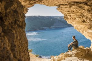 Gozo, île de Malte, jeune homme dans une grotte regardant l'océan et la baie de Ramla, de l'intérieur de la grotte Tal Mixta Gozo